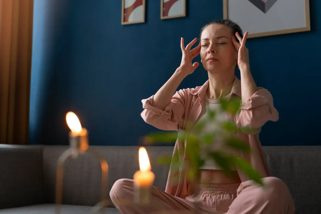 A person sitting calmly in a softly lit room, taking a quiet moment for their own wellbeing